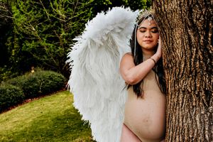 Angelic portrait session with white feathered wings against natural outdoor backdrop.