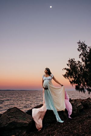 Dreamy maternity photoshoot at sunset by the ocean with flowing light blue dress.