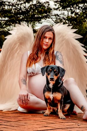 Woman in white with angel wings poses with black and tan dog on wooden deck.