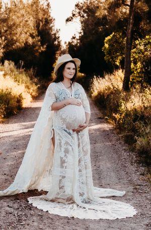 A flowing white lace maternity dress photographed in golden sunlight on a dirt path.