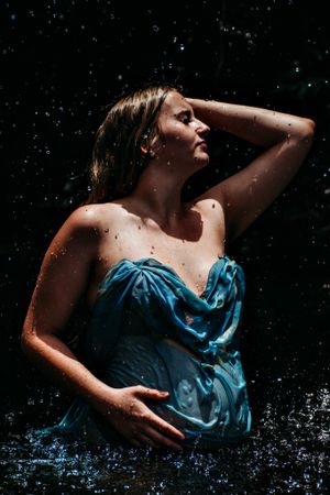 Artistic water portrait in blue fabric against dark background with water droplets.