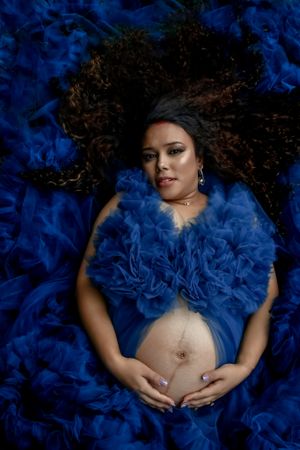Artistic maternity portrait with blue tulle against dark background.