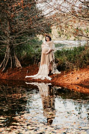 Ethereal maternity photo shoot by a reflective pond with autumn foliage.