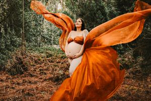 Flowing orange fabric creates dramatic movement in outdoor maternity photography.