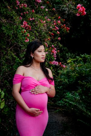 Maternity photo featuring bright pink dress against flowering garden background.