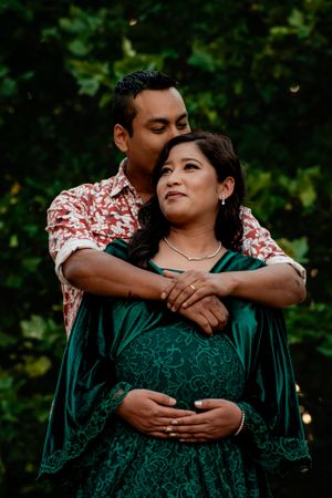 Intimate maternity portrait session in emerald green dress against garden backdrop.