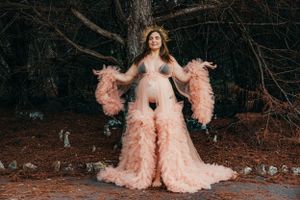 Elegant maternity photos featuring flowing pink gown in forest setting.