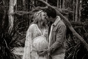 Intimate black and white maternity photo of couple embracing in forest setting.
