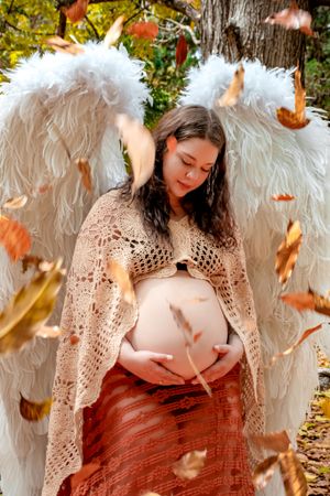 Angel wing maternity photography with falling autumn leaves in natural outdoor setting.
