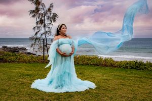 Flowing light blue dress billows in the wind against a dramatic purple sunset sky.