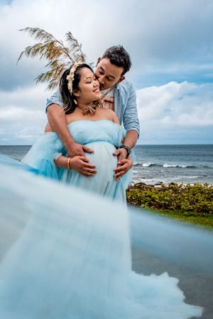 Romantic beachside photoshoot with flowing turquoise dress against ocean backdrop.