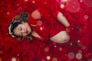 Dreamy maternity portrait with red bokeh lights and soft focus effects.