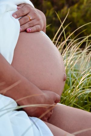 Close-up shot of a pregnant belly in white clothing against natural grass background.