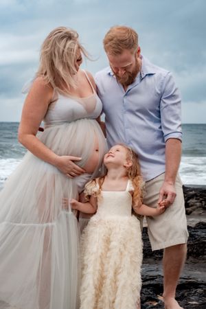 Family beach portrait with white flowing dress against ocean backdrop.