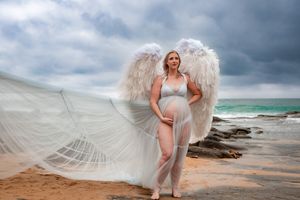 Dramatic beach maternity photos with flowing white fabric against stormy coastal scenery.