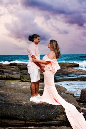 Flowing peach dress catches wind on rocky coastline with crashing waves.