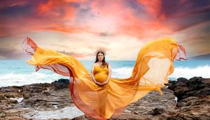 Flowing orange fabric billows dramatically against a rocky coastal sunset landscape.