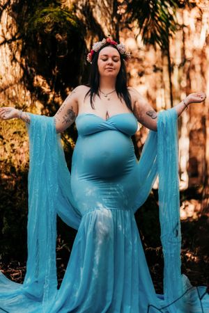 Maternity photoshoot in forest setting with flowing turquoise blue dress at sunset.