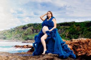 Long blue dress flows elegantly along rocky coastal shoreline at sunset.