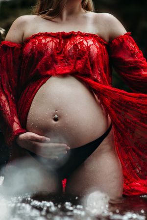 Artistic maternity photo featuring red lace fabric and dramatic smoke effects against dark background.