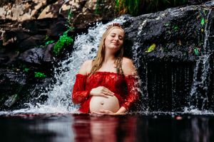 Dramatic maternity portrait at a natural waterfall with flowing red fabric.