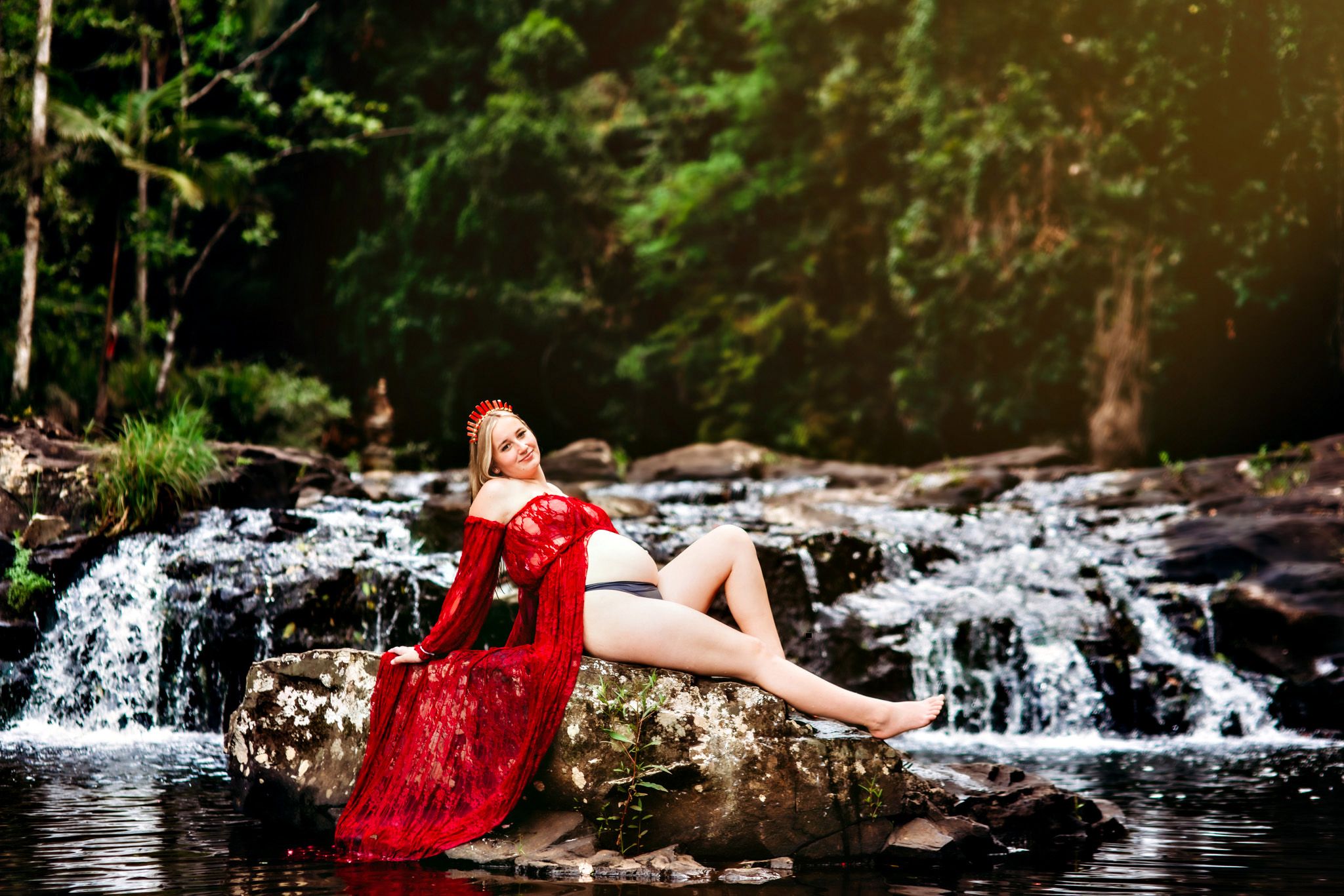 Maternity photography session by cascading waterfall with red flowing dress.