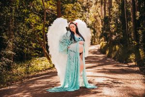 Outdoor maternity photography with flowing aqua dress on sunlit forest path.