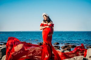 Flowing red dress contrasts dramatically against blue ocean and sandy beach landscape.