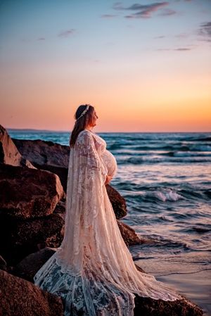 White lace dress flowing in the wind against a sunset beach backdrop with crashing waves.