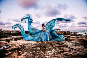 Flowing blue fabric dances in the wind against a rocky coastal landscape.