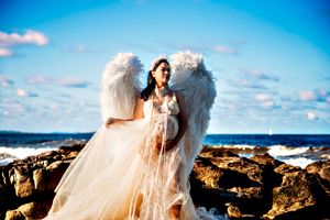 Angel wings and white dress silhouetted against a bright blue ocean backdrop.