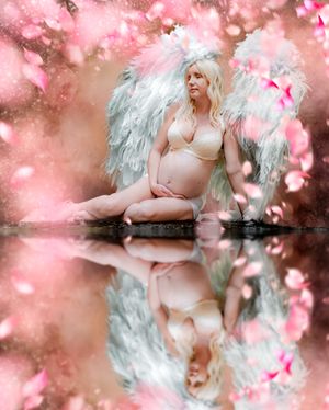 Ethereal maternity photoshoot with pink cherry blossoms and reflections in water.
