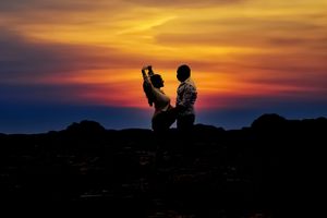 Silhouettes against dramatic orange and purple sunset sky over rocky landscape.