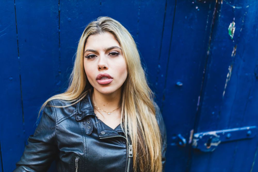 Beatriz Sonnewend looking stunning and seductive at the camera against a dark blue door in a black leather jacket