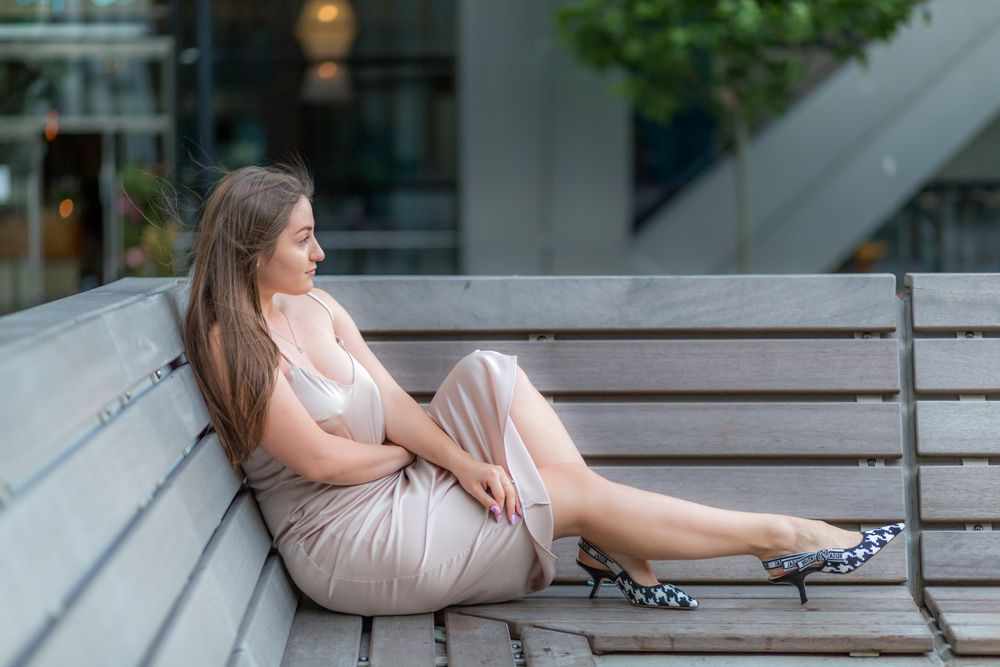 Gorgeous Ukrainian model, Stasia, sat on a bench with her leg straight out wearing a gold dress