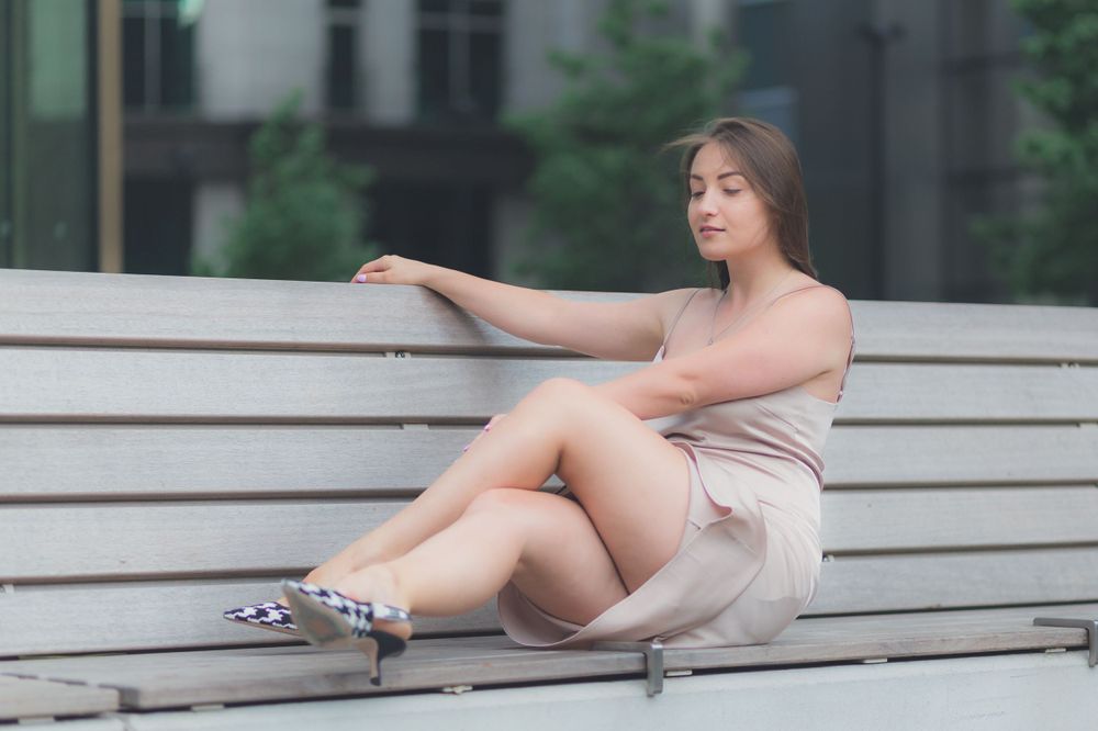 Stunning Ukrainian model, Stasia, sat on a bench with her legs up and dark hair blowing, wearing golden dress