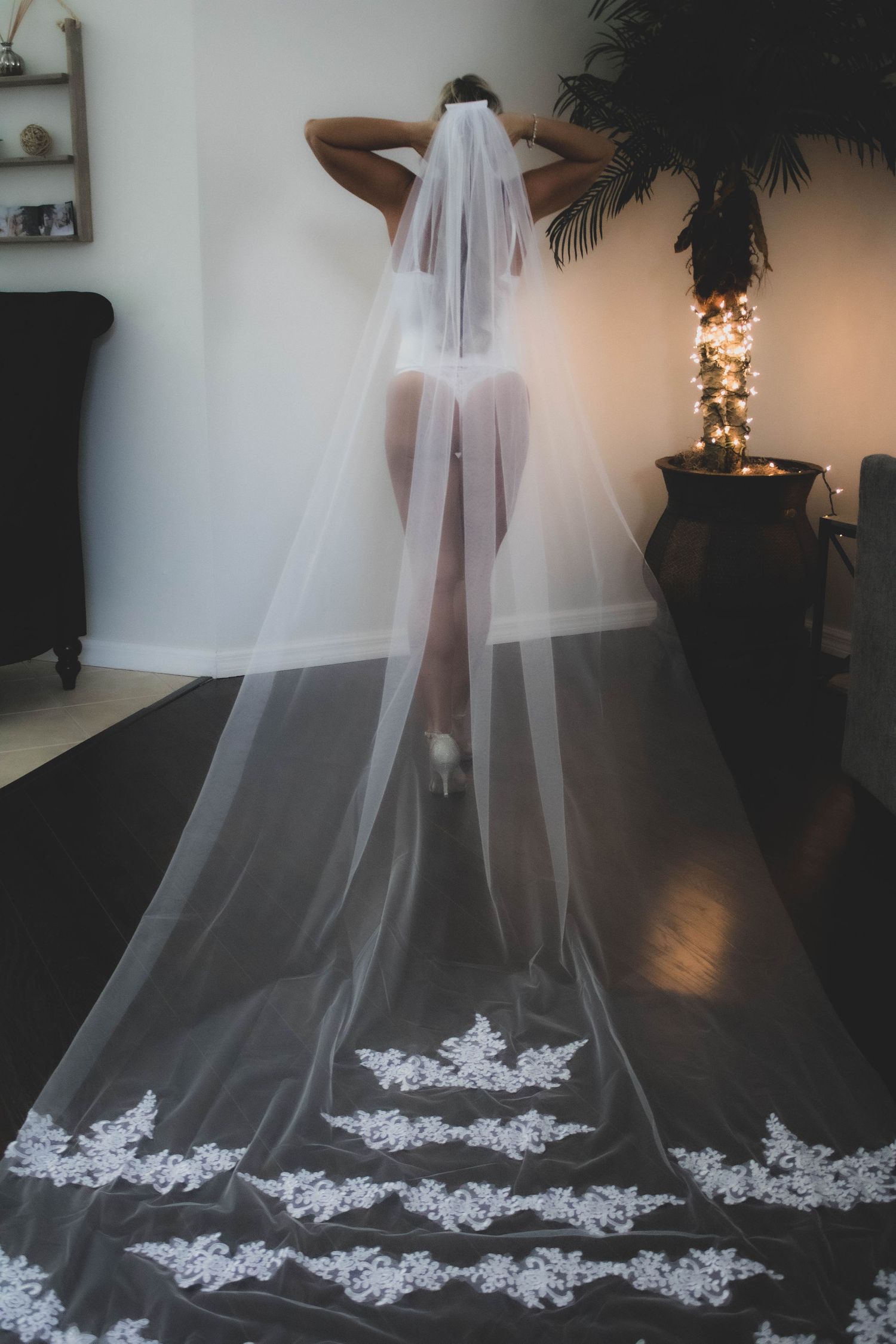 A bridal boudoir photo featuring an elegant long white veil with lace detailing against dark flooring.