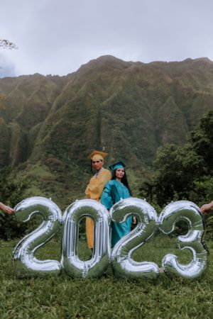 Silver 2023 number balloons displayed on grass with mountains in the background.