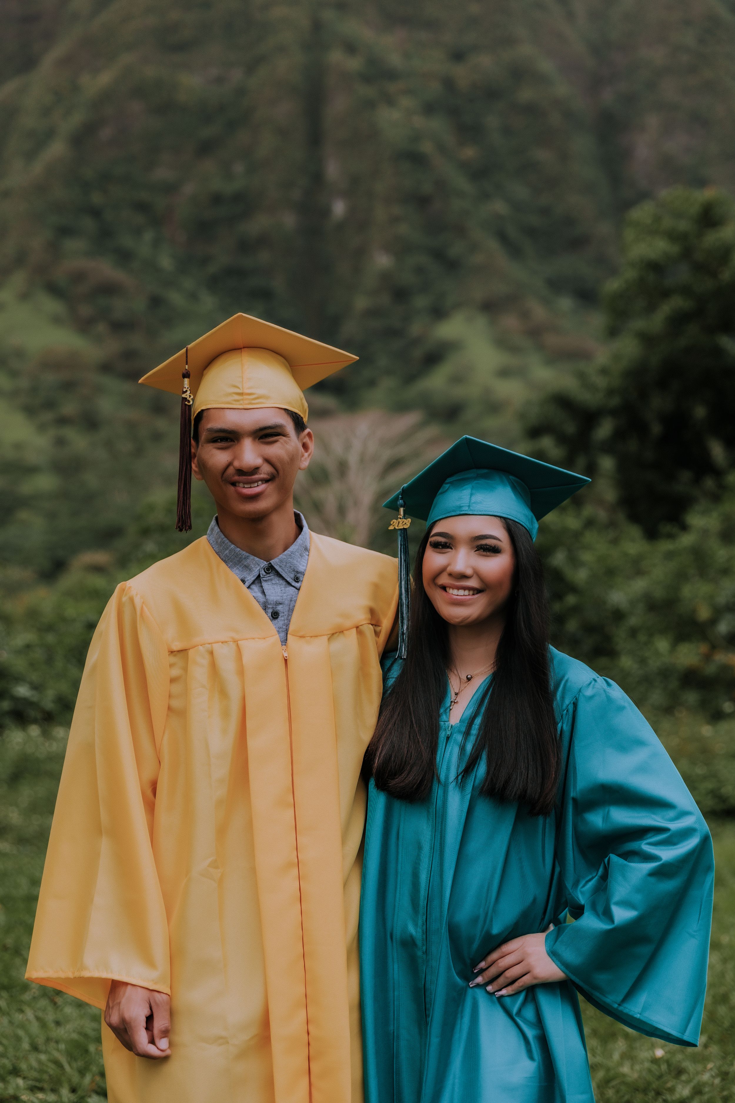 Graduates in yellow and teal gowns posing together in a lush mountain setting.