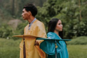 Graduates celebrating in bright yellow and teal gowns with mountains in the background.