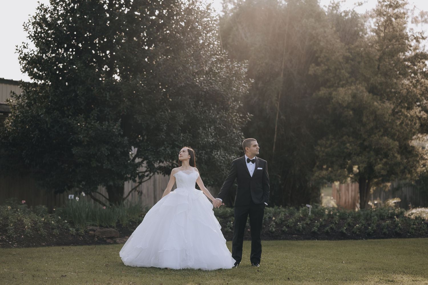 Couple in wedding attire walking together on landscaped lawn during golden hour.