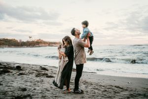 A family enjoys a sunset moment together on a dramatic black sand beach with crashing waves.