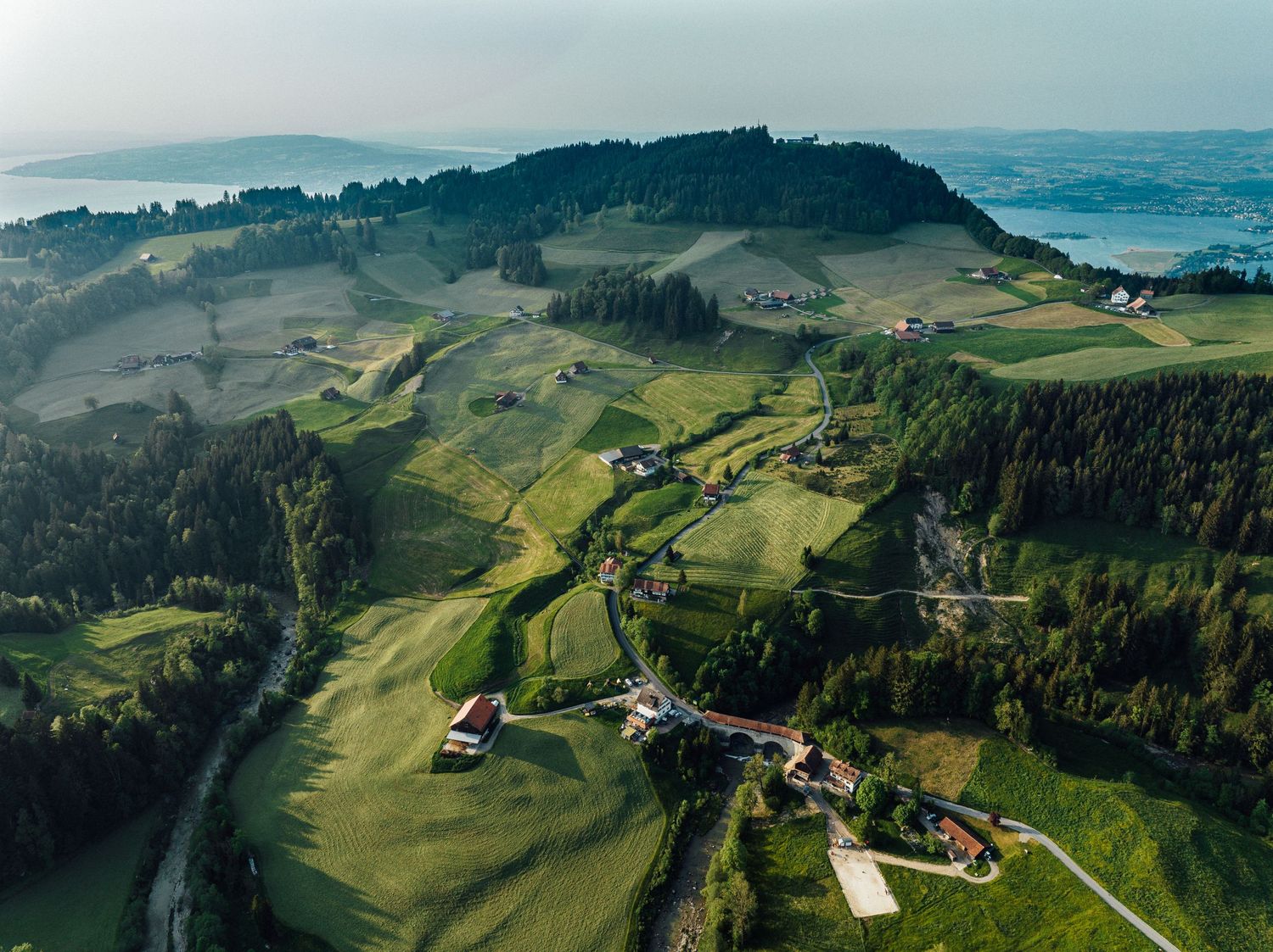 Aerial view of a misty mountainous landscape with scattered buildings and green rolling hills.