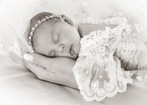 Black and white portrait of sleeping newborn wearing lace dress and floral headband.