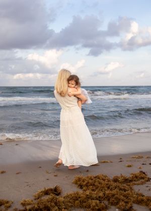 A tender moment between parent and child on a beach at sunset with crashing waves in the background.