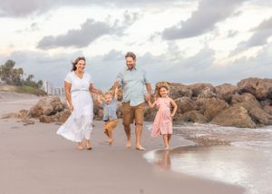 Happy family running together on beach at sunset wearing white and pink outfits.