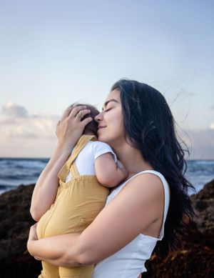 Tender moment captured between parent and child against ocean backdrop at sunset.