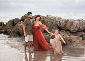 Family of three enjoying beach time together with rocky coastline backdrop.