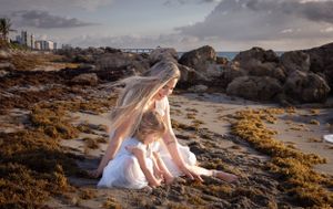 Woman in white dress with child exploring rocky beach landscape at sunset.