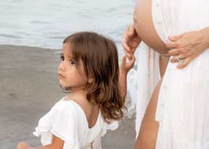 Small child in white dress holding adult's hand while walking on beach.